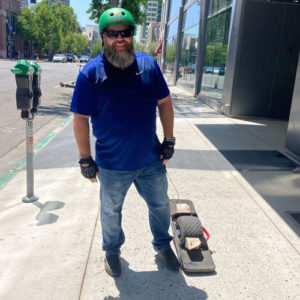 Man stands with Onewheel on the sidewalk outside an office building