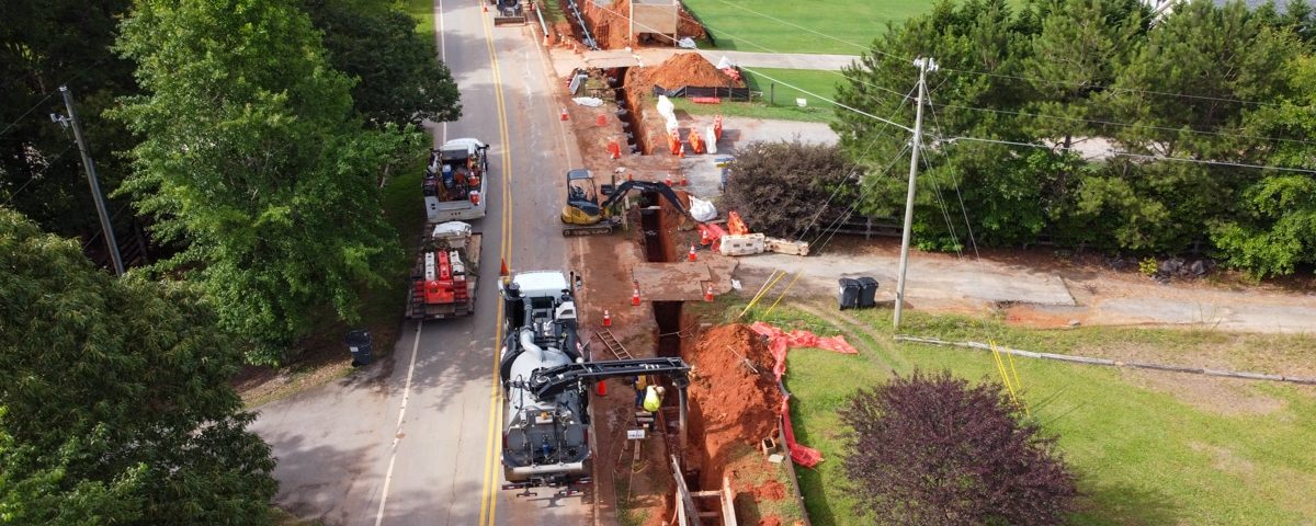 construction vehicles and workers along road with pipeline