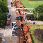construction vehicles and workers along road with pipeline