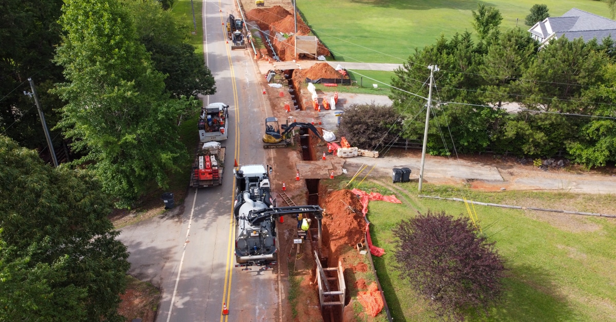 construction vehicles and workers along road with pipeline