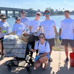 Group of people pose with shopping cart full of litter in front of bay and bridge