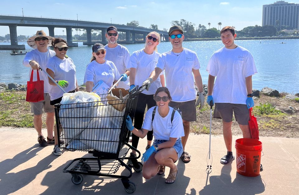 Group of people pose with shopping cart full of litter in front of bay and bridge