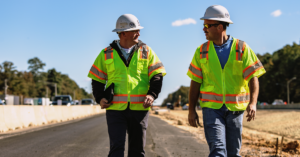 Two NXL staff in yellow vests and hard hats walking along a road on a project site