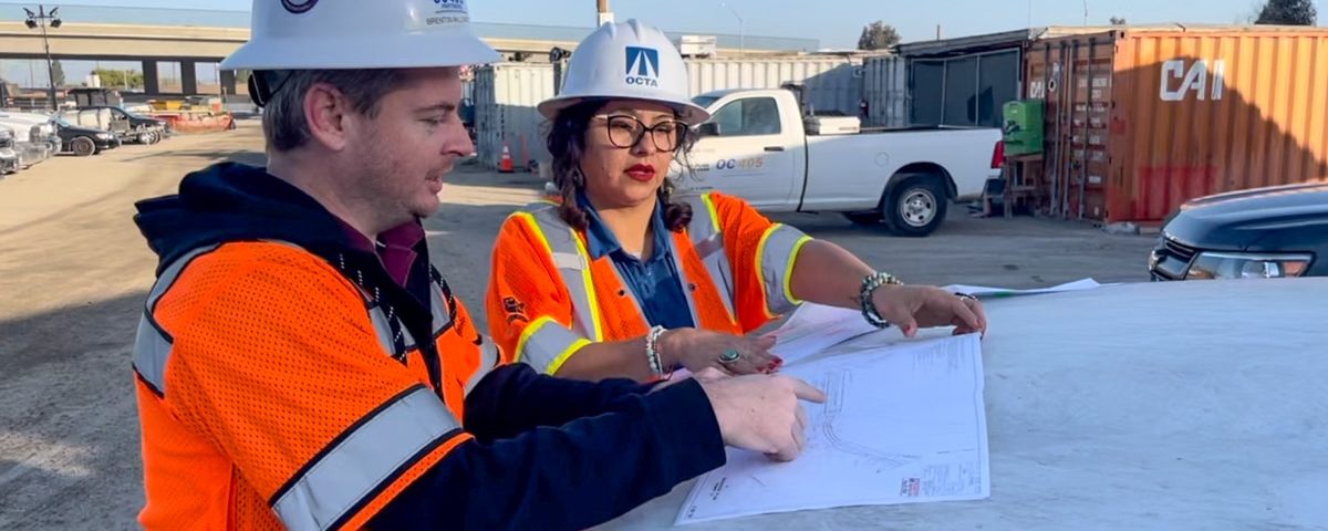 Two people in safety equipment review plans at construction site