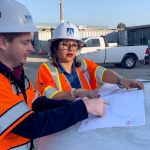 Two people in safety equipment review plans at construction site