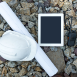 Stock photo of hard hat, blueprints, iPad, and radio on top of rocks