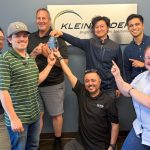 Group of people stand in front of Kleinfelder logo sign with glass award
