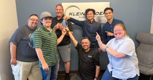 Group of people stand in front of Kleinfelder logo sign with glass award