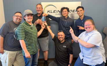 Group of people stand in front of Kleinfelder logo sign with glass award