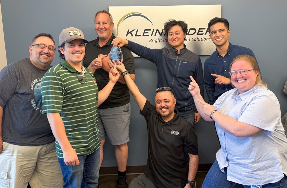 Group of people stand in front of Kleinfelder logo sign with glass award