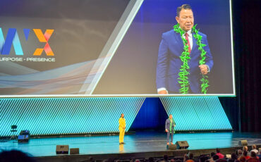 Vic Bianes speaking at PWX conference on large stage with large screen in background