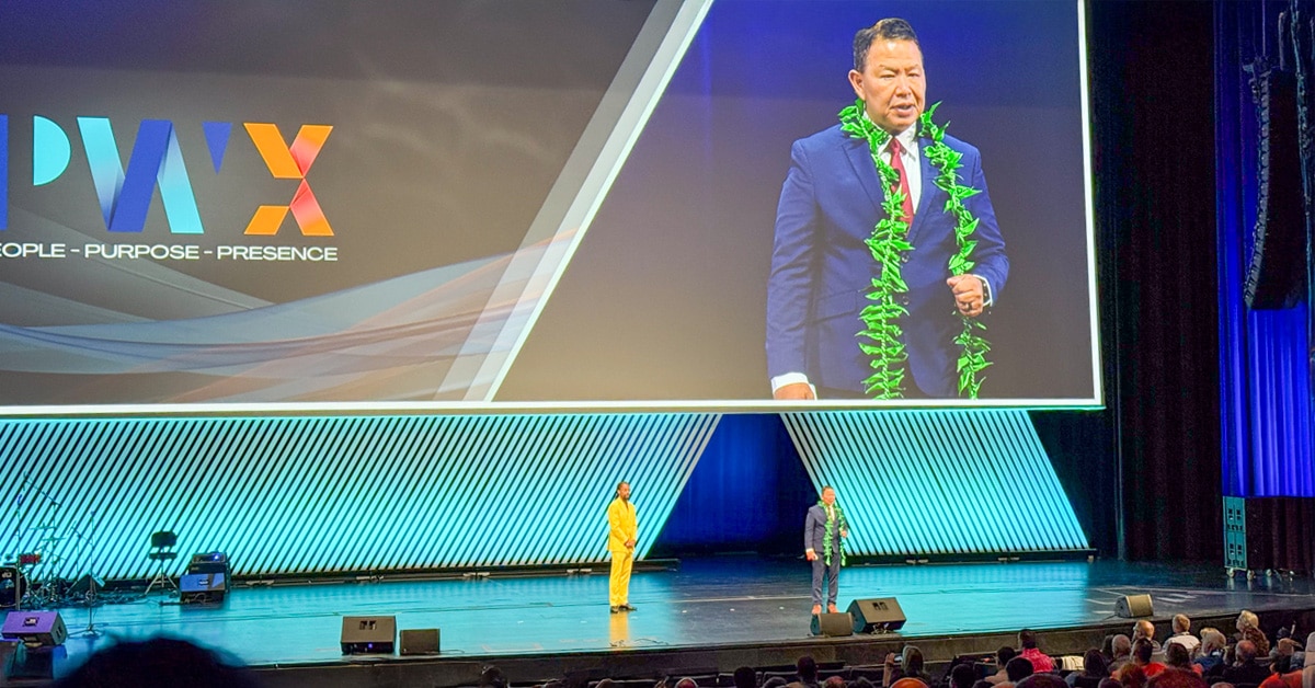 Vic Bianes speaking at PWX conference on large stage with large screen in background