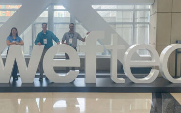 Three people stand with WEFTEC conference sign