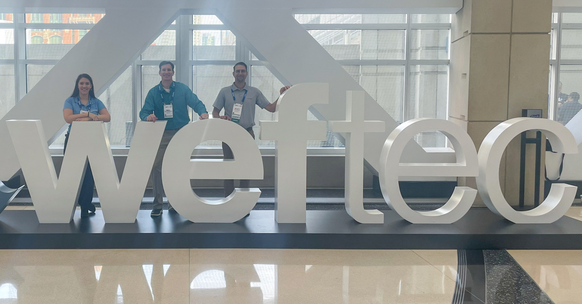 Three people stand with WEFTEC conference sign