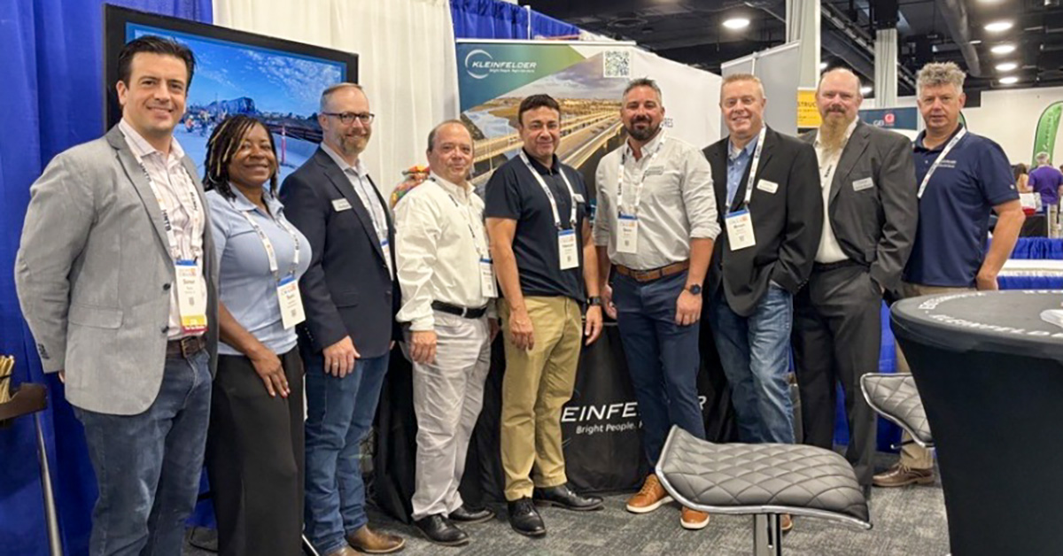 group posing for photo in front of exhibit booth at CMAA conference