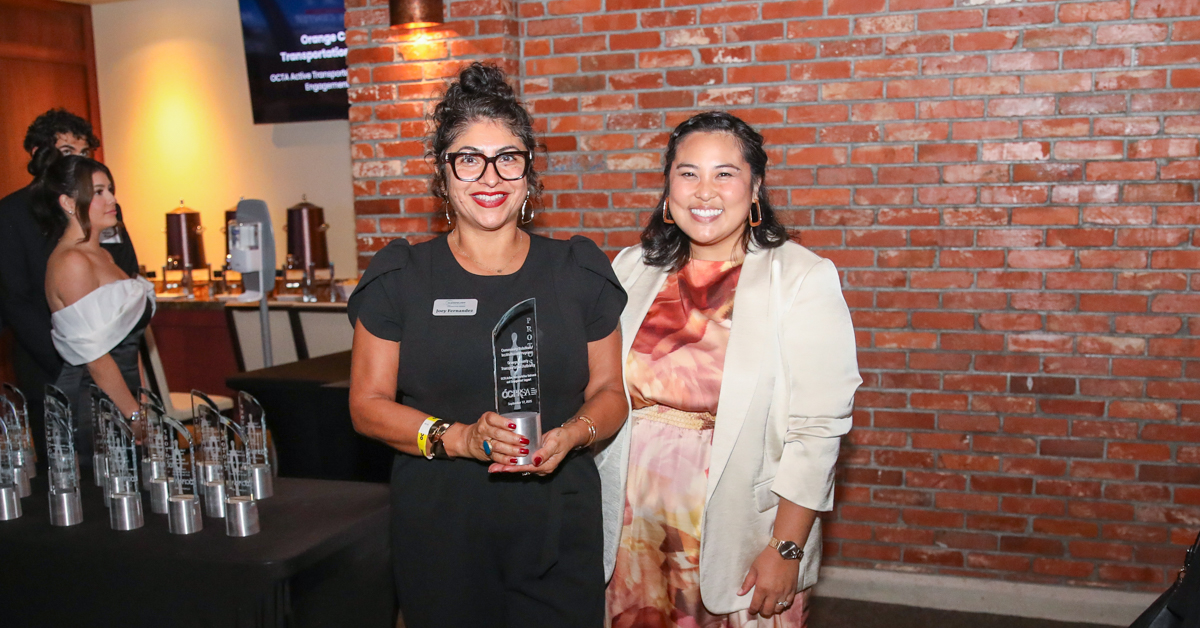 two people pose with glass award in front of brick wall