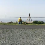 Kleinfelder surveyor sits next to surveying equipment and looks at water
