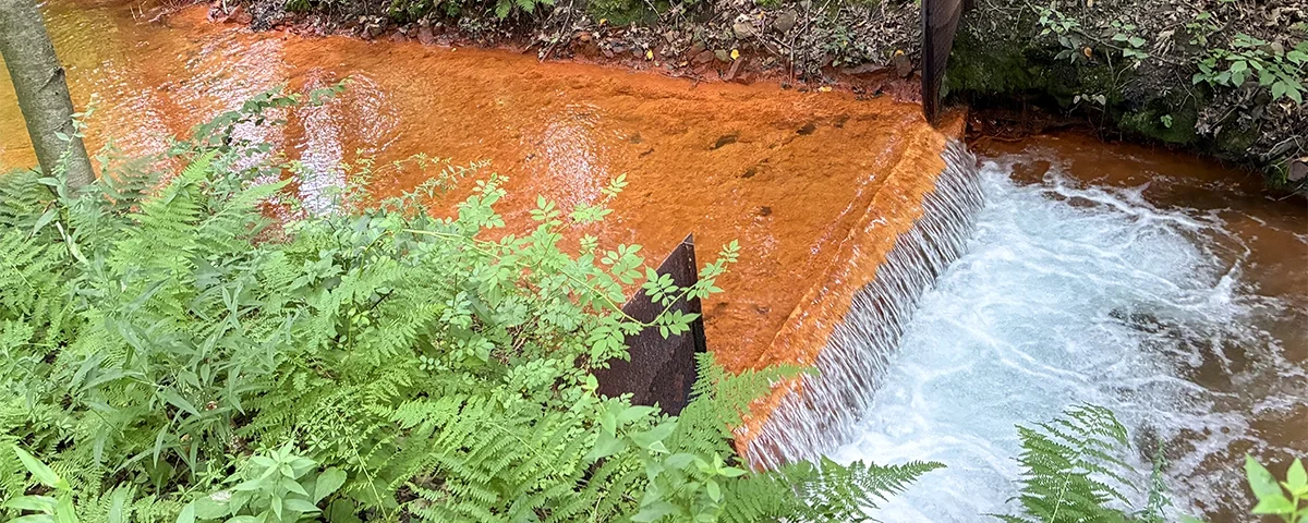 Shamokin Creek Scott Mine discharge creek flowing over small waterfall with orange coloring and surrounding green plants