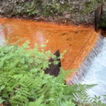 Shamokin Creek Scott Mine discharge creek flowing over small waterfall with orange coloring and surrounding green plants